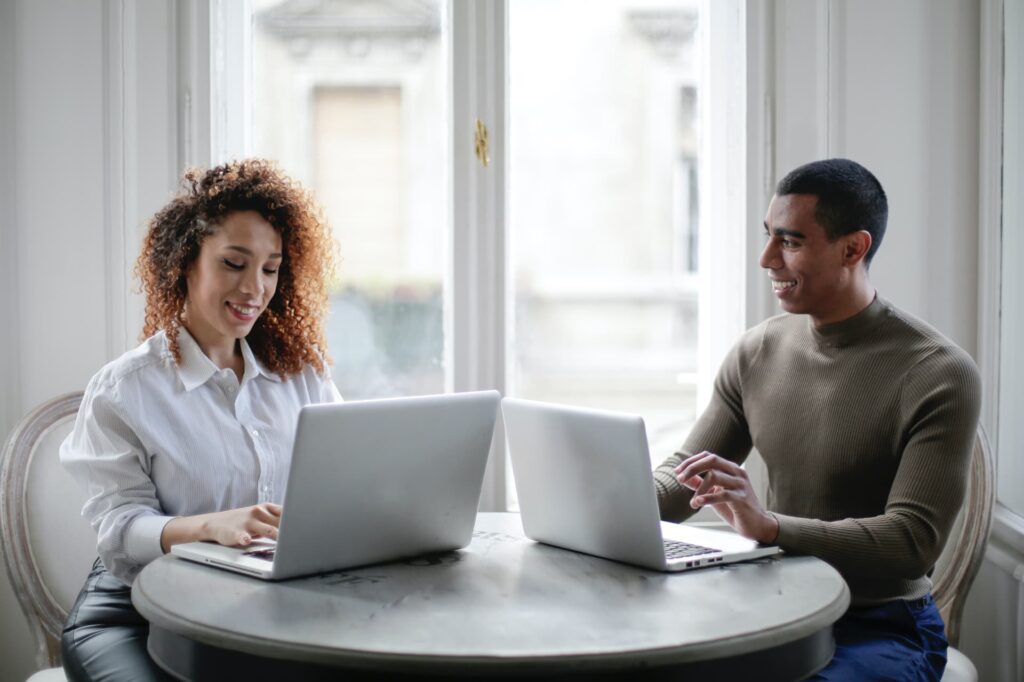 cheerful-young-couple-using-laptops-while-sitting-at-table